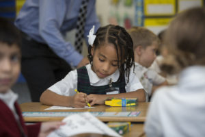 Child drawing coloring at school desk.