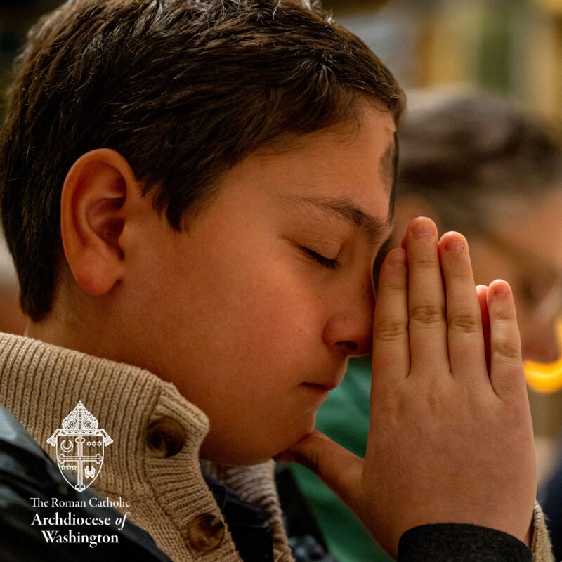 Ash Wednesday young boy praying with Ash Cross on forehead