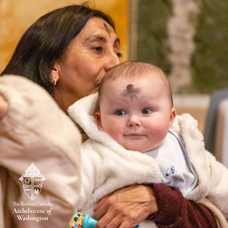 Woman holding baby with Ash Cross on forehead of both woman and baby.